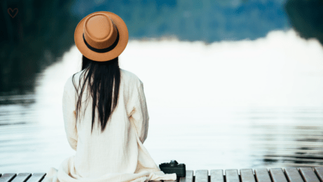 Žena sedící zády u klidné vodní hladiny, v tichém zastavení a spočinutí.